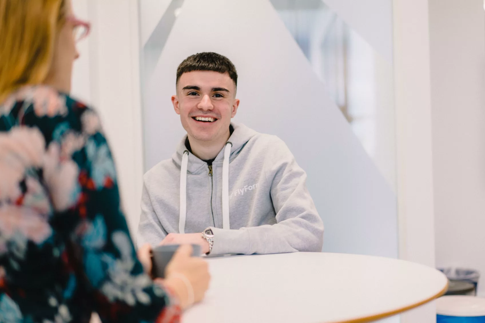 A male team member smiles widely while sitting across the table from another team member