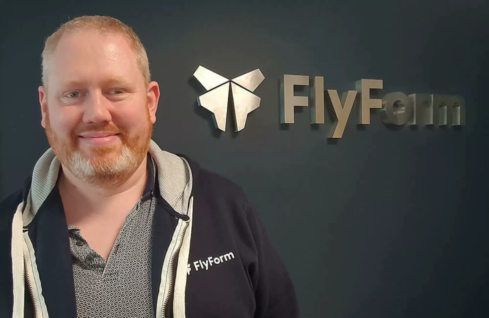 A headshot of FlyForm's IT Manager, Tom Collis in front of the FlyForm logo.