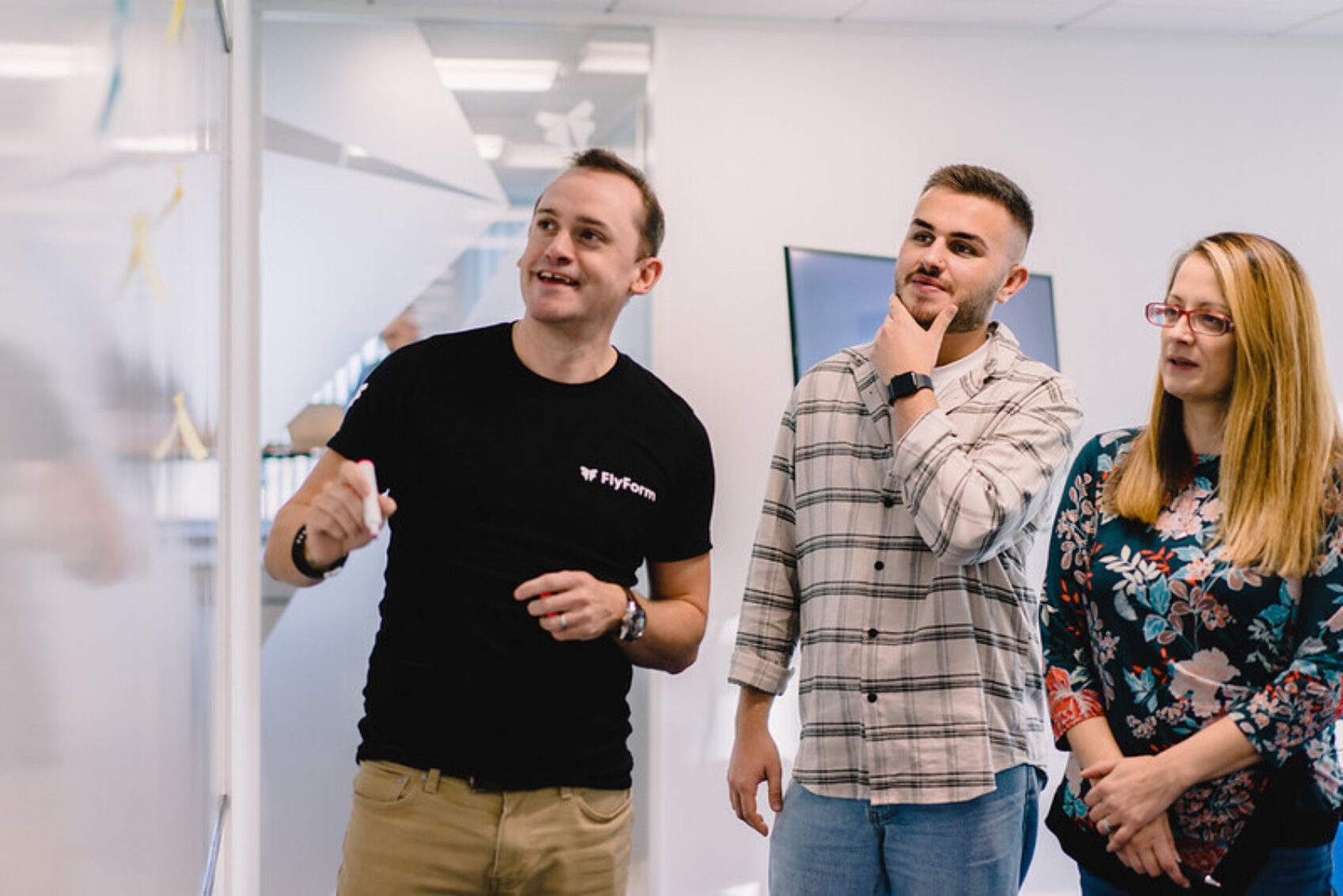 3 team members discuss work in front of a whiteboard