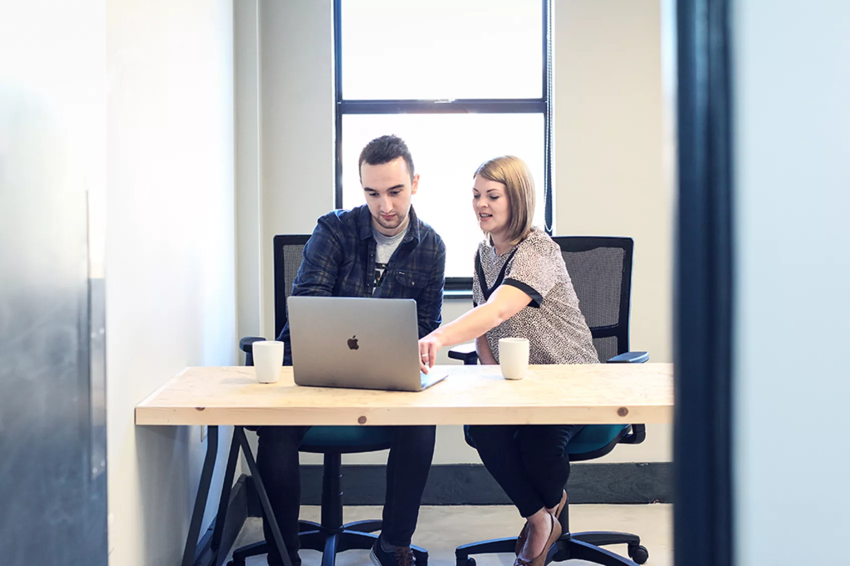 2 team members discuss work in front of a laptop