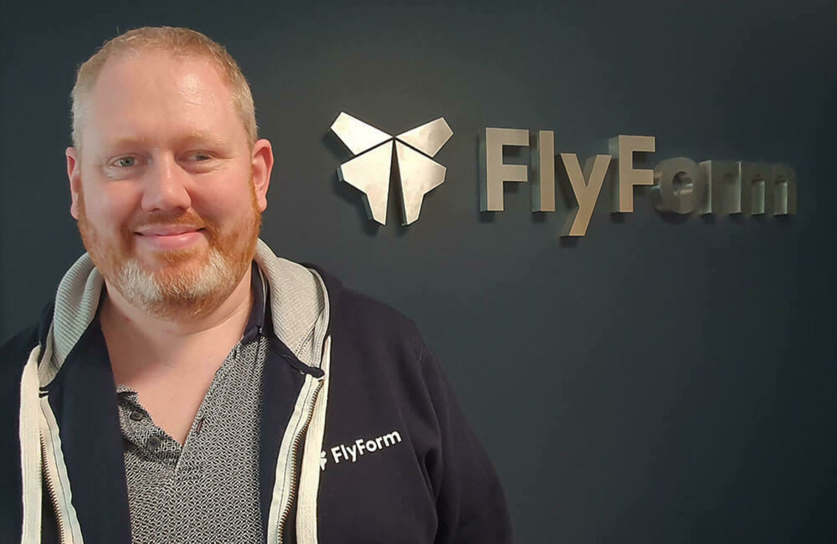 A headshot of FlyForm's IT Manager, Tom Collis in front of the FlyForm logo.